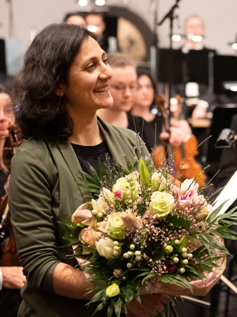 Farzia Fallah nimmt Beifall und Blumenstrauß nach der Uraufführung vor dem Orchester stehend entgegen. 