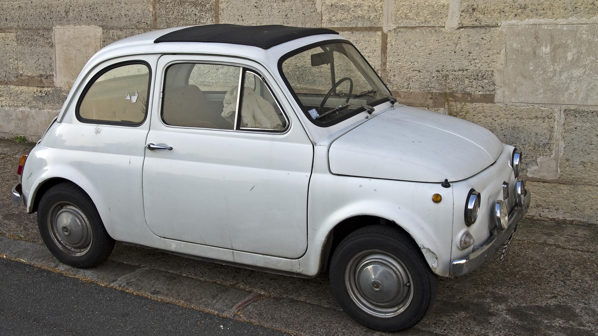 Ein weißer Fiat 500 steht in einer Straße. Ein weißer Fiat 500 steht in einer Straße.