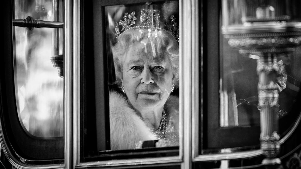 Die Queen ist durch das Fenster ihrer Kutsche zu sehen und schaut direkt in die Kamera. Sie trägt ein diamantenbesetztes Diadem.