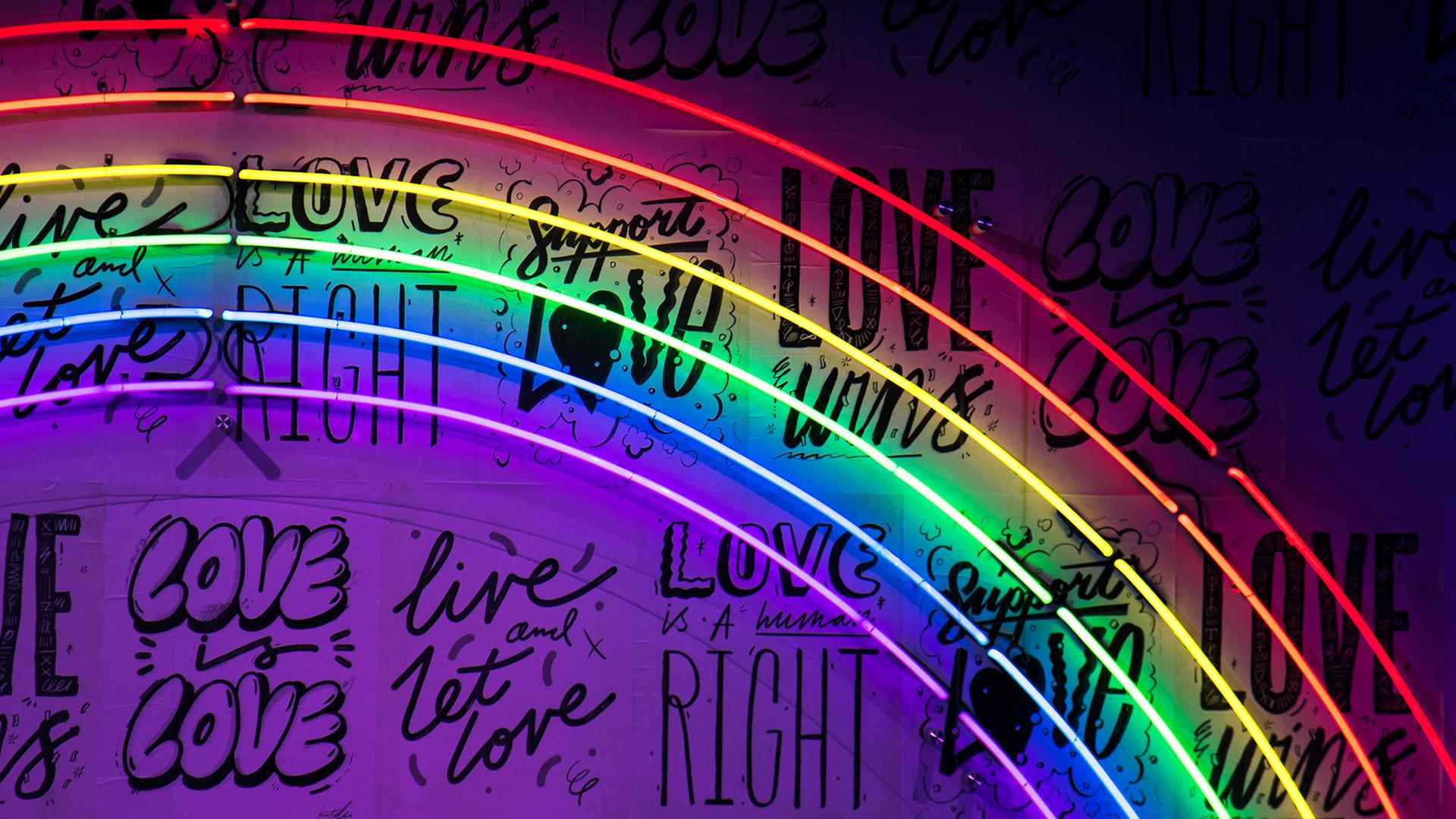 Ein Regenbogen aus Leuchtröhren. An der Wand stehen die Wörter: Love oder Right in verschiedenen Schriftzügen. 