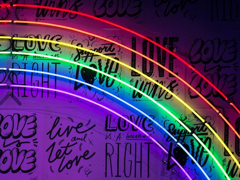 Ein Regenbogen aus Leuchtröhren. An der Wand stehen die Wörter: Love oder Right in verschiedenen Schriftzügen. 