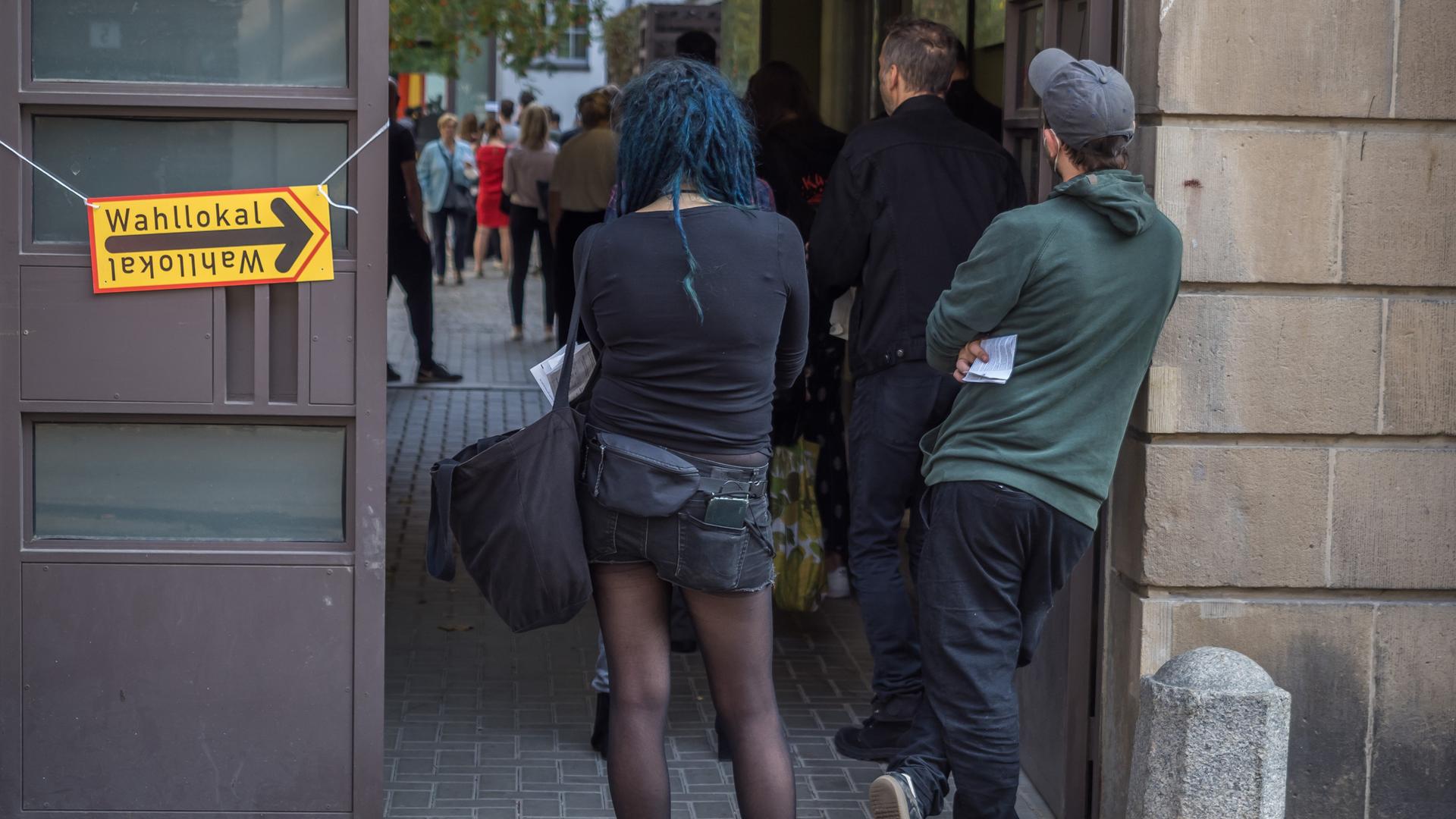 Menschen warten in einer Schlange vor einem Wahllokal im Berliner Stadtteil Prenzlauer Berg darauf, ihre Stimmen zu Bundestags- und Abgeordnetenhauswahl sowie zur Wahl der Bezirksvertretungen abgeben zu dürfen. Am Ende der Schlange steht eine Frau mit blauen Haaren und schwarzer Kleidung.