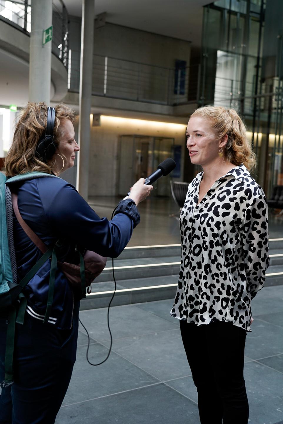 Eine Frau hält einer anderen Frau ein Mikrofon hin und interviewt sie. Eine Frau hält einer anderen Frau ein Mikrofon hin und interviewt sie.