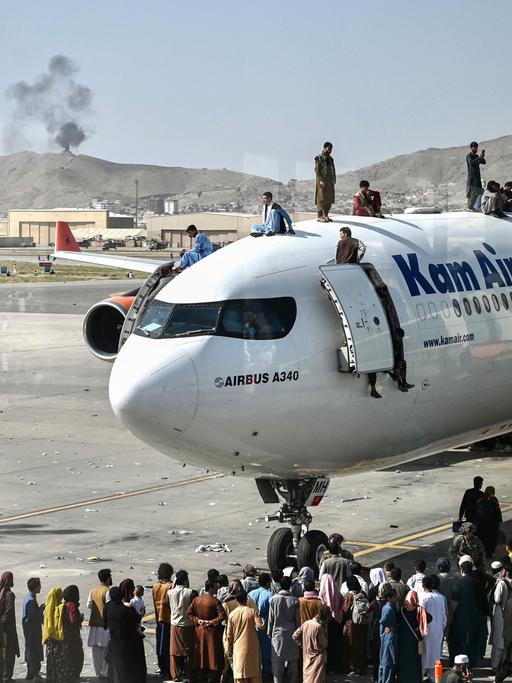 Afghanische Menschen klettern auf ein Flugzeug auf dem Flughafen in Kabul im August 2021. Sie versuchen verzweifelt zu fliehen, weil die Taliban die Macht übernommen haben.