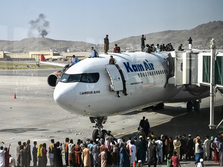 Afghanische Menschen klettern auf ein Flugzeug auf dem Flughafen in Kabul im August 2021. Sie versuchen verzweifelt zu fliehen, weil die Taliban die Macht übernommen haben.