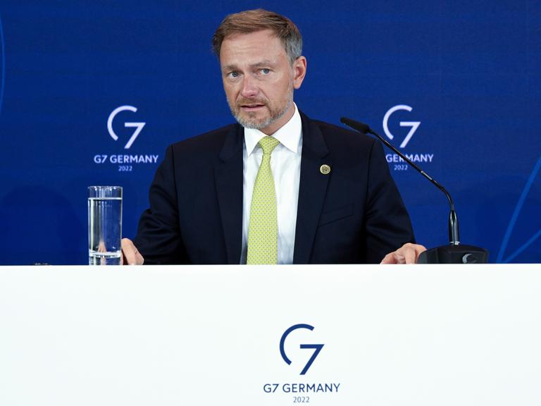 Christian Lindner sitzt an einem Tisch mit Mikrofon und redet, im Hintergrund ist das Logo der G7 zu sehen.