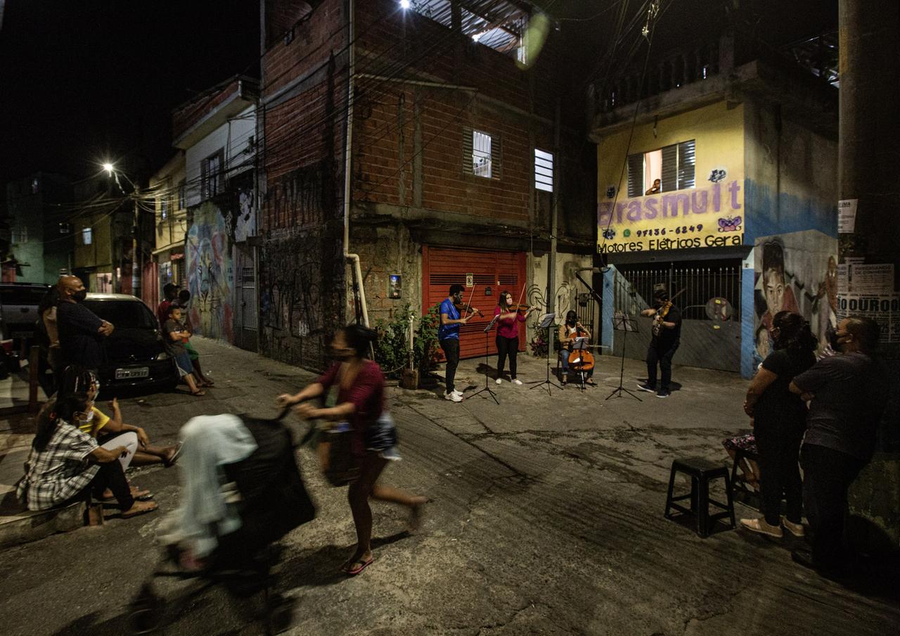 Ein Streichquartett spielt abends inmitten von Zuschauern und Passanten an einer Straßenkreuzung in der Favela Heliopolis in Sao Paulo.