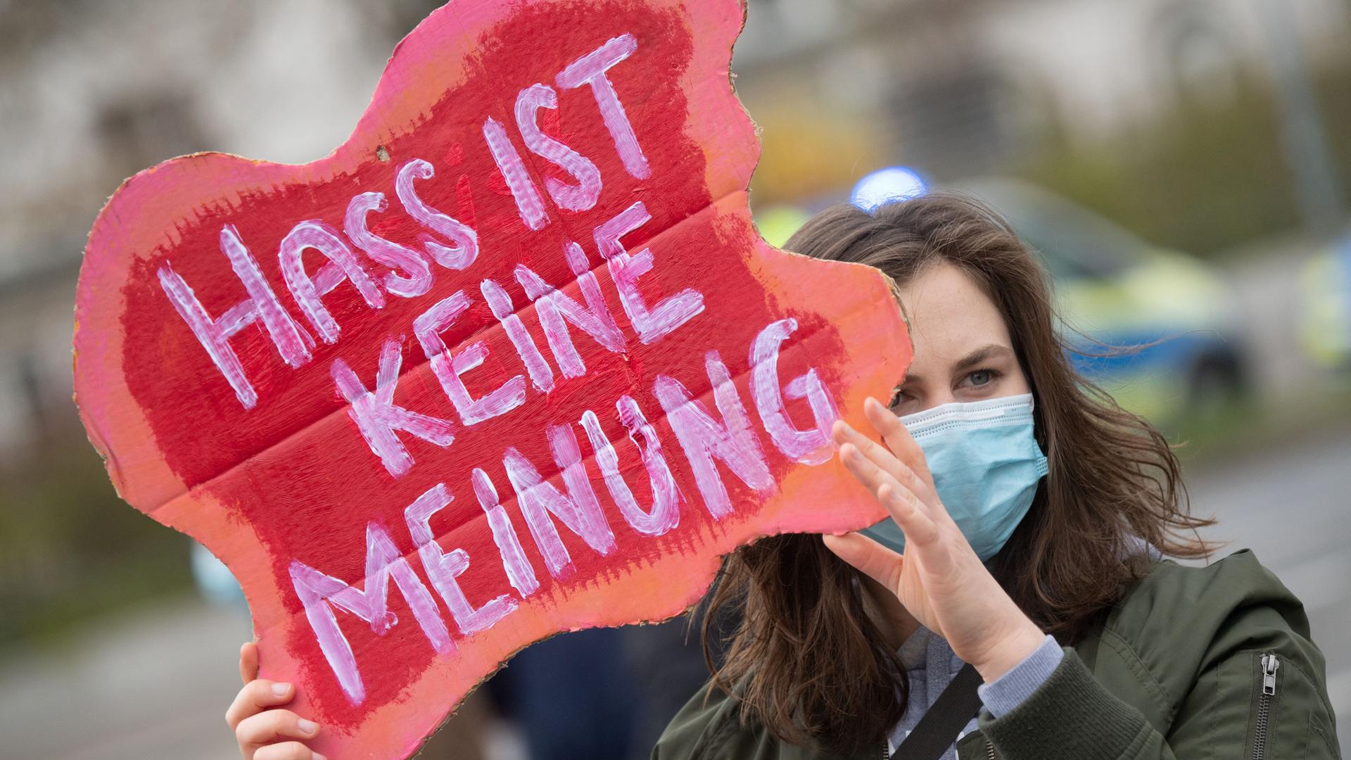 Eine Teilnehmerin einer Gegenveranstaltung protestieren in Greifswald mit dem Schriftzug «Hass ist keine Meinung» in die Kamera. Eine Teilnehmerin einer Gegenveranstaltung protestieren in Greifswald mit dem Schriftzug «Hass ist keine Meinung» in die Kamera.