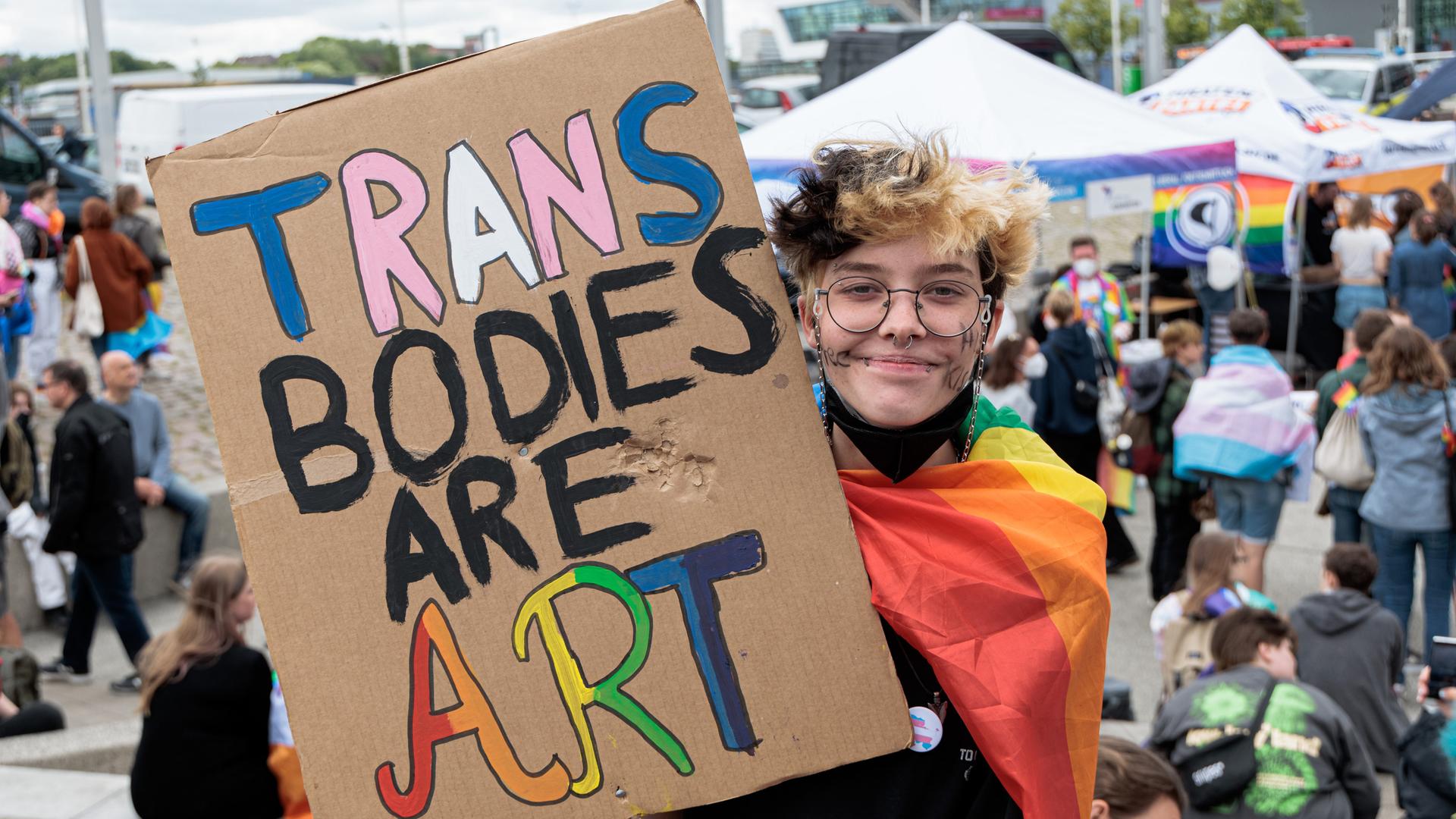 Noah hält auf der Demonstration zum Christopher Street Day (CSD) im Juli 2022 in Kiel ein Schild mit der Aufschrift "Trans Bodies Are Art" Noah hält auf der Demonstration zum Christopher Street Day (CSD) im Juli 2022 in Kiel ein Schild mit der Aufschrift "Trans Bodies Are Art"