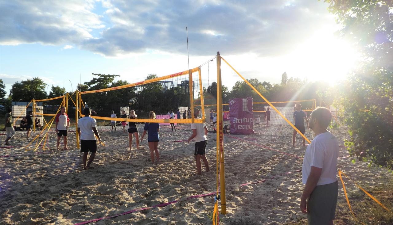 Mehrere Personen spielen an einem sommerlichen Abend Beachvolleyball. 