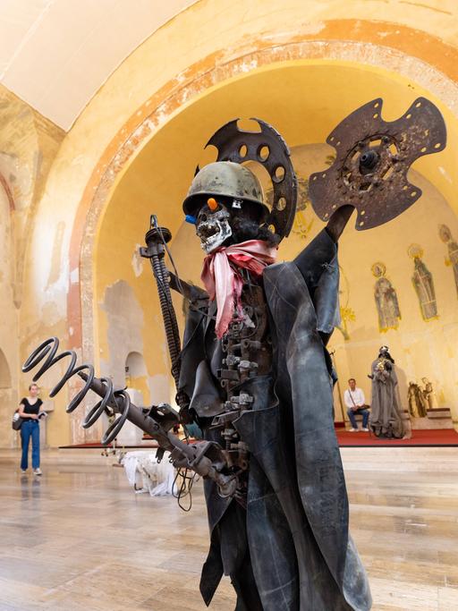Die aus Maschinenteilen, einem Stahlhelm und Tüchern zusammengesetzte lebensgroße Figur eines Soldaten steht zusammen mit anderen Skulpturen in einer ehemaligen Kirche.