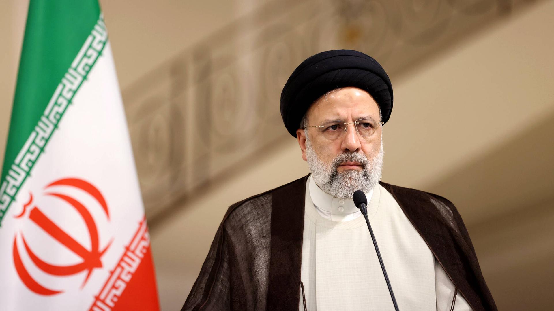 Ebrahim Raisi, Präsident der Islamischen Republik Iran, vor einem Mikrofon und neben einer iranischen Flagge Ebrahim Raisi, Präsident der Islamischen Republik Iran, vor einem Mikrofon und neben einer iranischen Flagge