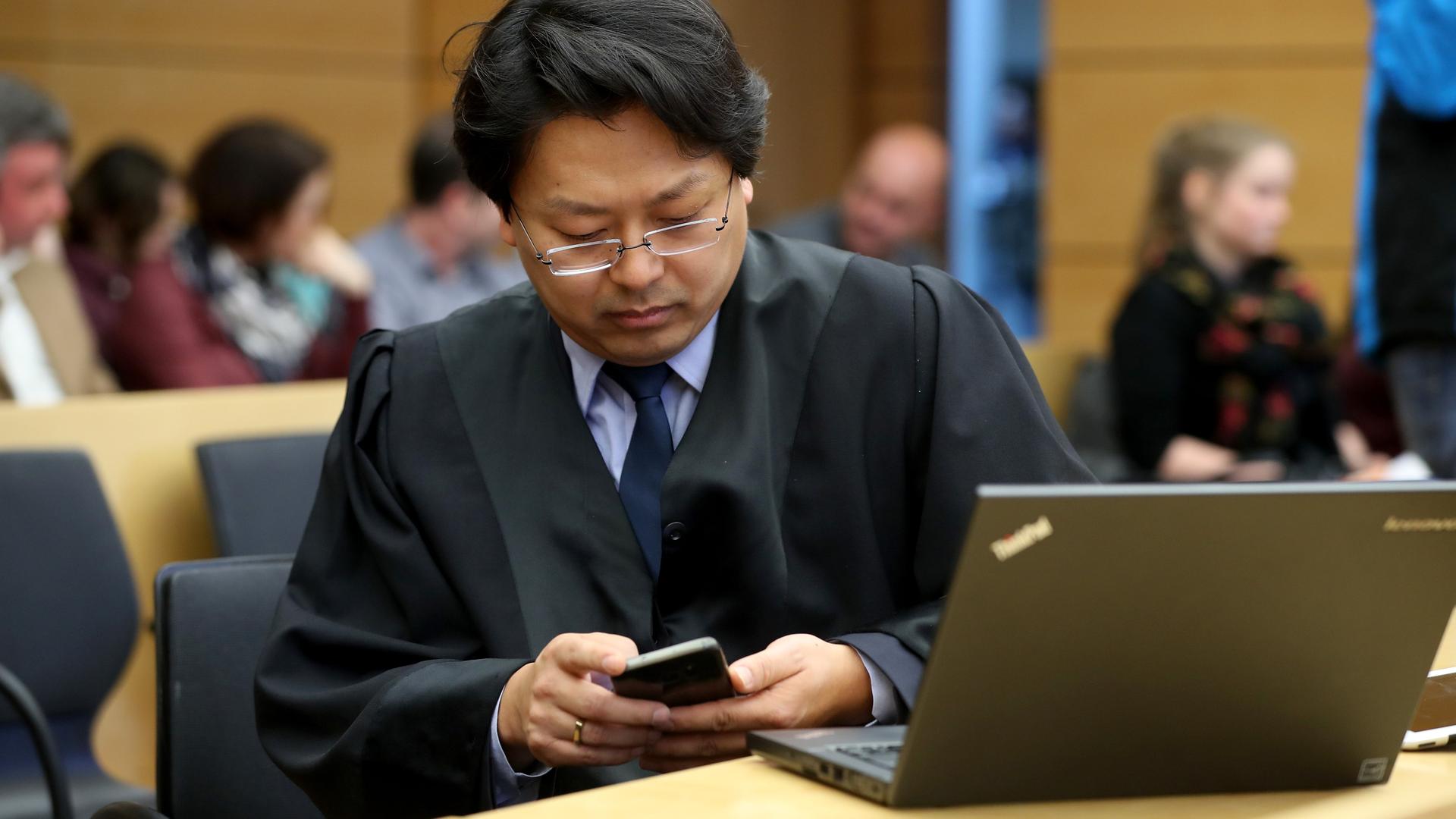 Jun Chan-jo sitzt in seiner Anwaltsrobe im Gerichtssaal und schaut auf sein Smartphone.