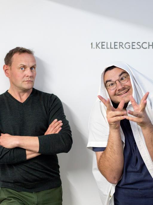 Devid Striesow und Axel Rahnisch stehen vor einer weißen Wand und schneiden Grimassen.