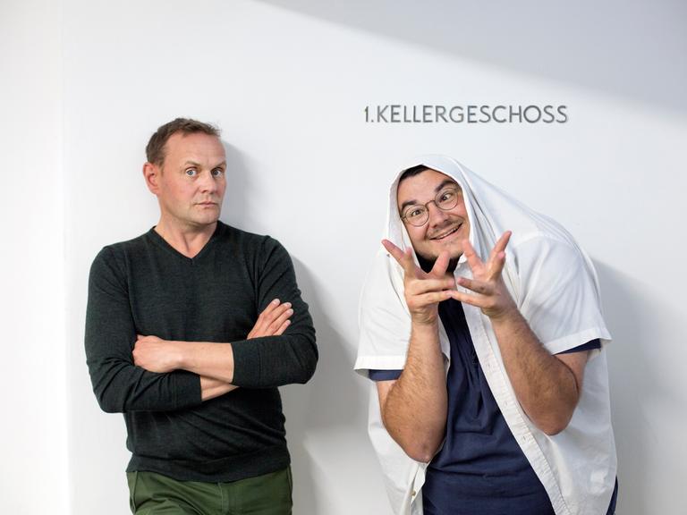 Devid Striesow und Axel Rahnisch stehen vor einer weißen Wand und schneiden Grimassen.