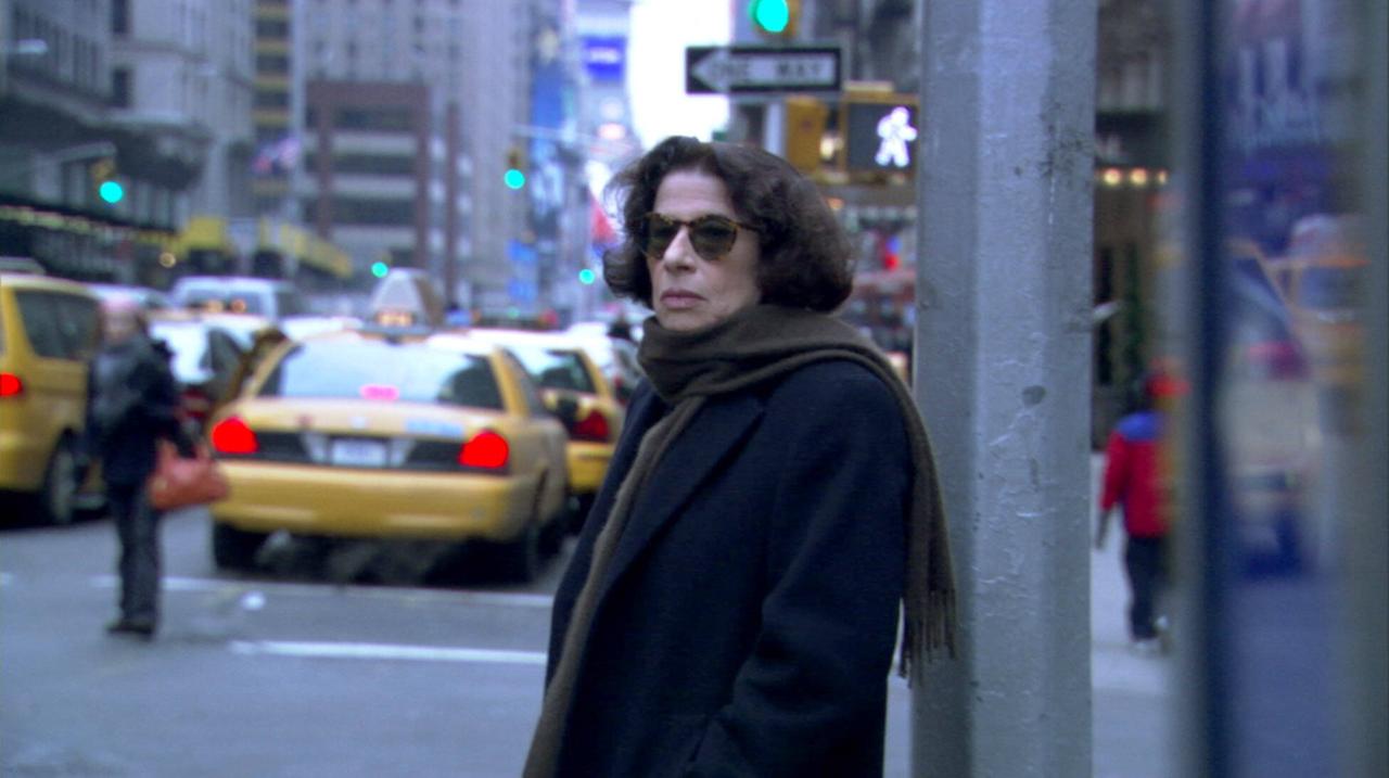 Fran Lebowitz steht in cooler Pose und mit Sonnenbrille an einer New Yorker Straße, auf der Taxis fahren. Fran Lebowitz steht in cooler Pose und mit Sonnenbrille an einer New Yorker Straße, auf der Taxis fahren.