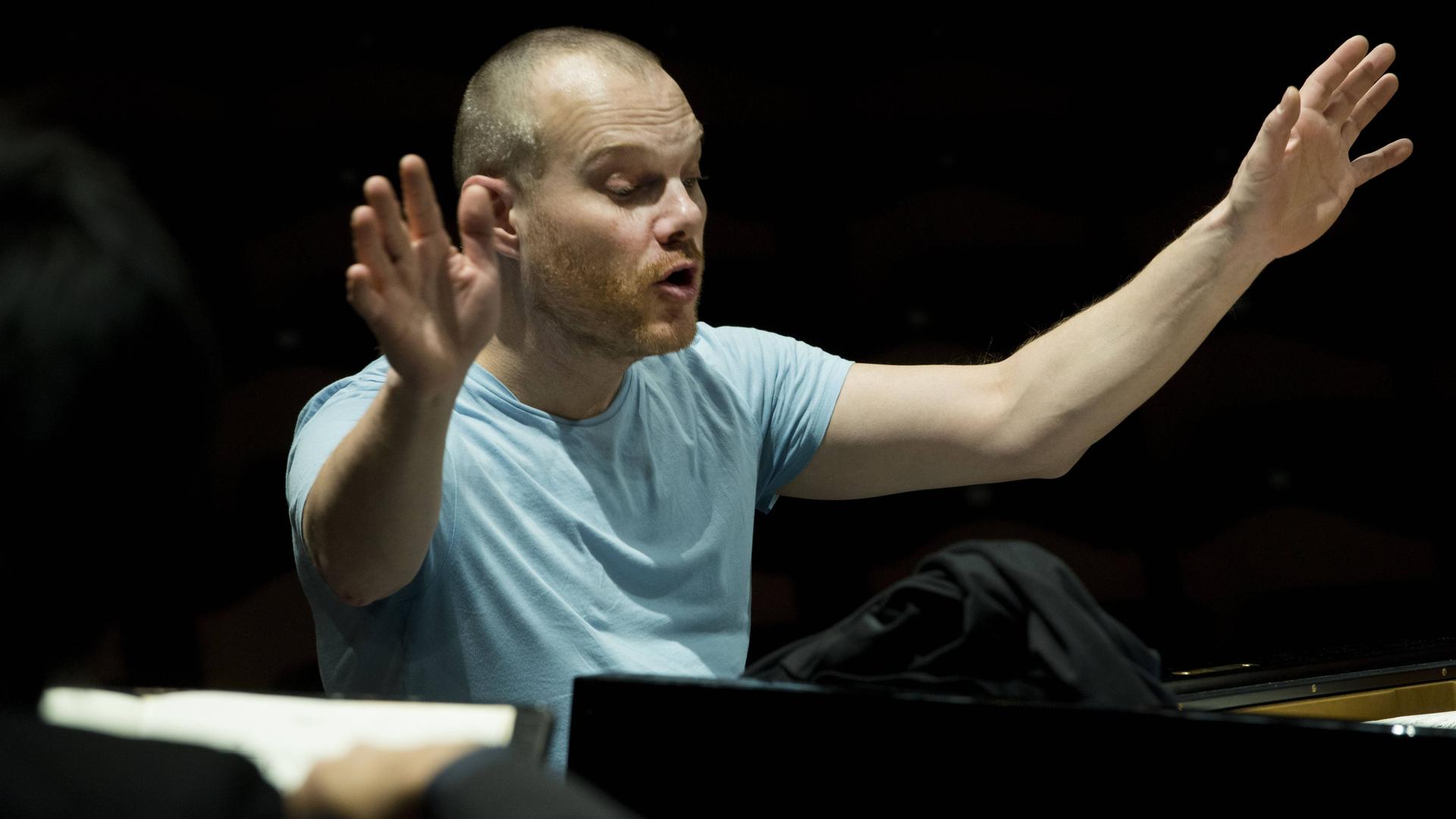 Ein Mann sitzt vor einem Piano und gestikuliert energisch. Ein Mann sitzt vor einem Piano und gestikuliert energisch.