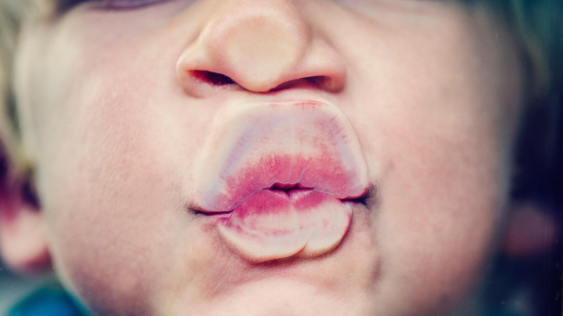 Ein Kind drückt Nase und Mund wie bei einem Kuss gegen eine Glasscheibe.