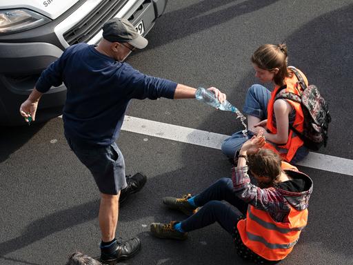 Ein Verkehrsteilnehmer schüttet bei einer Blockade der Letzten Generation einer Aktivistin Wasser über den Kopf.