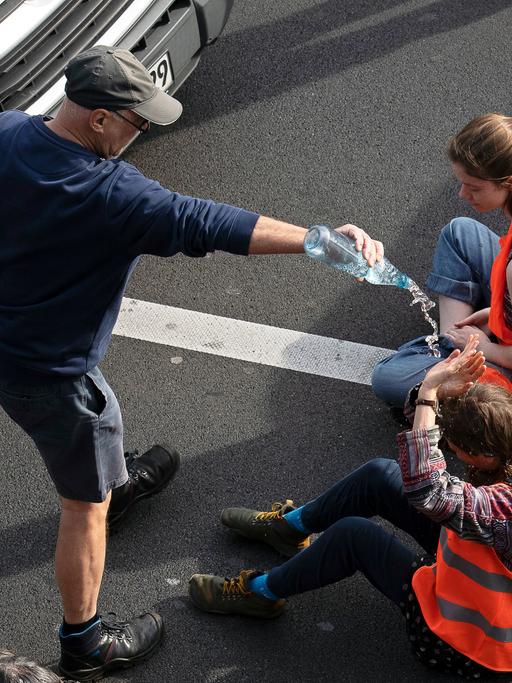 Ein Verkehrsteilnehmer schüttet bei einer Blockade der Letzten Generation einer Aktivistin Wasser über den Kopf.