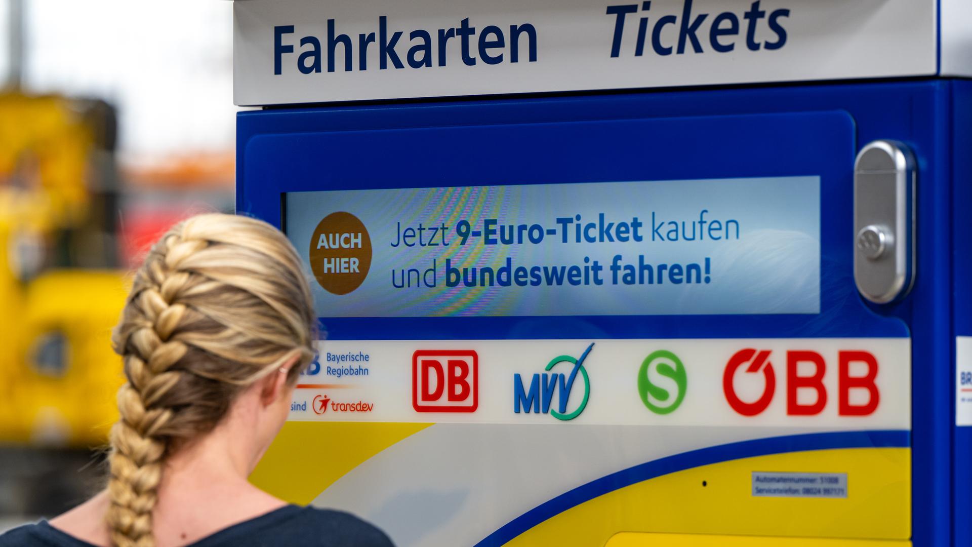 Eine junge Frau steht am Hauptbahnhof in München an einem Fahrkartenautomaten auf dem Werbung für das 9-Euro-Ticket zu sehen ist.