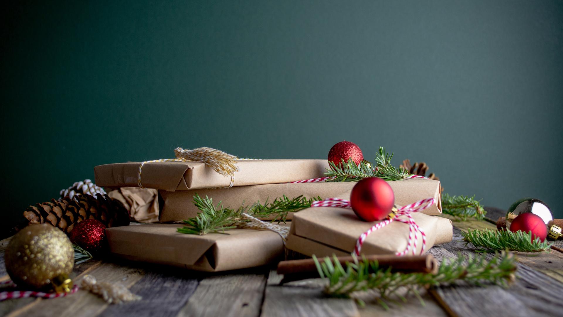 Verpackte Geschenke liegen vro einem grünen Hintergrun auf dem Holztisch.
