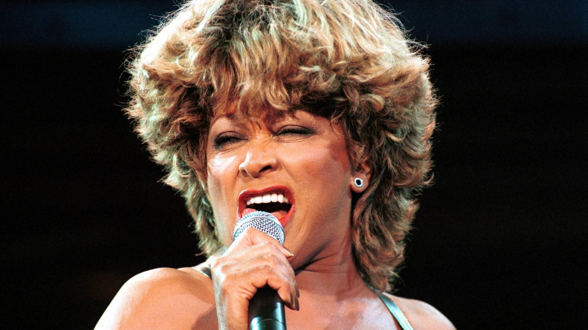 Tina Turner steht auf einer Bühne und singt in ein Mikrofon. Tina Turner steht auf einer Bühne und singt in ein Mikrofon.