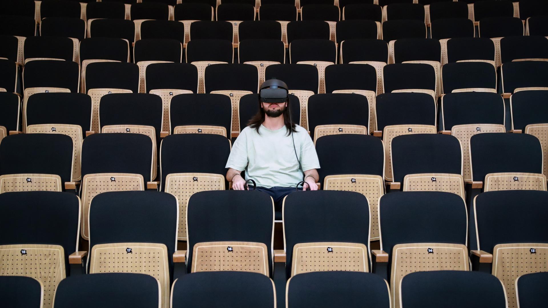 Ein Mann trägt eine VR-Brille und sitzt im Zuschauerraum eines Theaters.