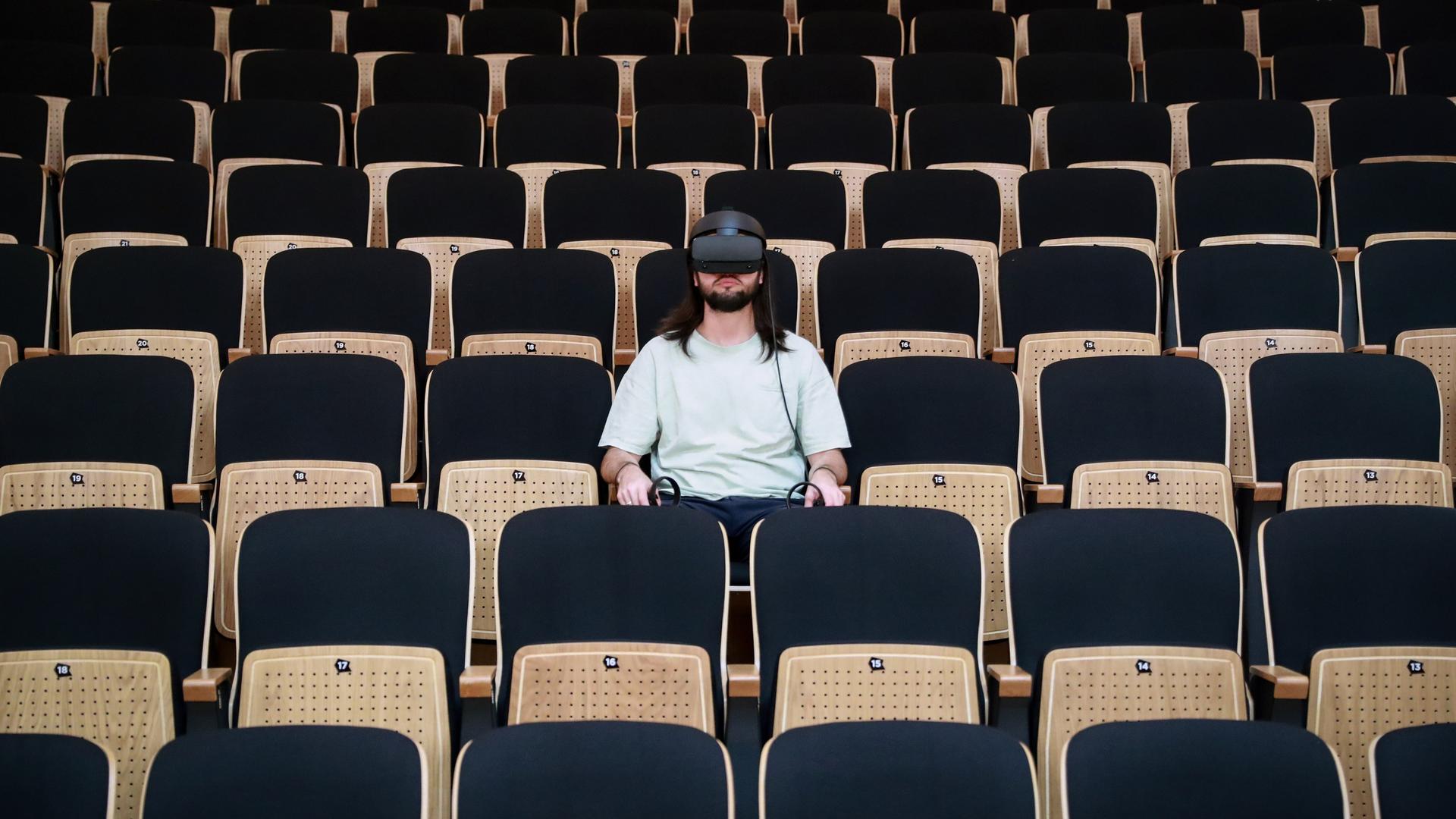 Ein Mann trägt eine VR-Brille und sitzt im Zuschauerraum eines Theaters. Ein Mann trägt eine VR-Brille und sitzt im Zuschauerraum eines Theaters.
