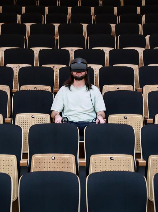 Ein Mann trägt eine VR-Brille und sitzt im Zuschauerraum eines Theaters.