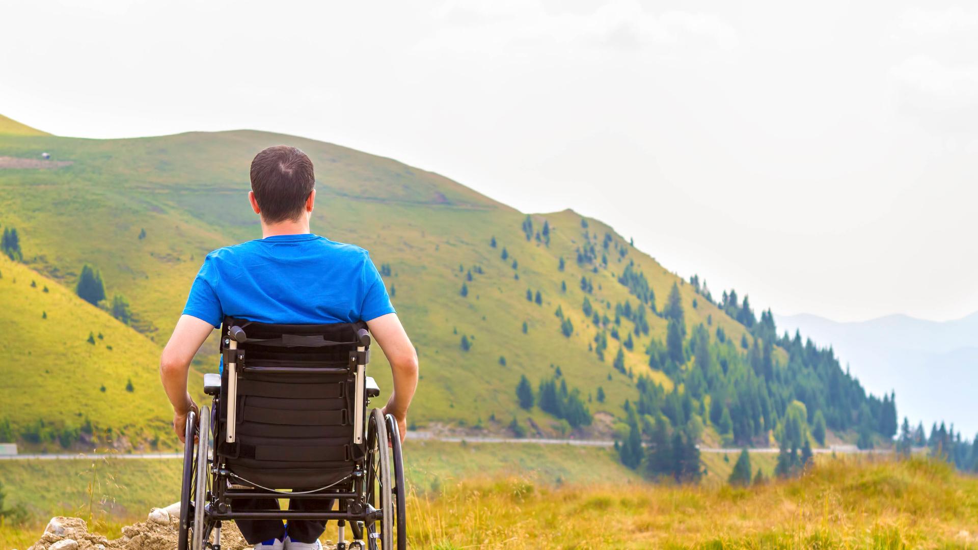 Ein Rollstuhlfahrer blickt auf einen Berg Ein Rollstuhlfahrer blickt auf einen Berg