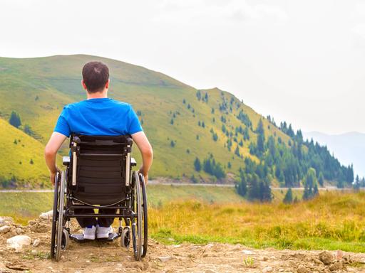 Ein Rollstuhlfahrer blickt auf einen Berg