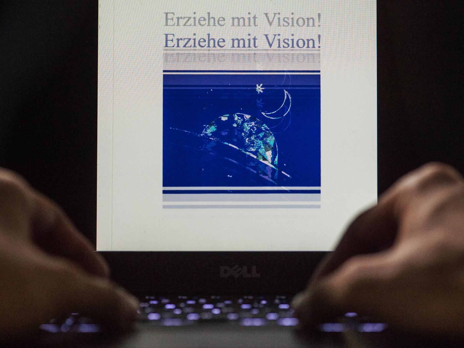 Nahaufnahme von zwei männlichen Händen an einem Laptop. Auf dem beleuchteten Display steht die Aufschrift "Erziehe mit Vision!" doppelt untereinander.
