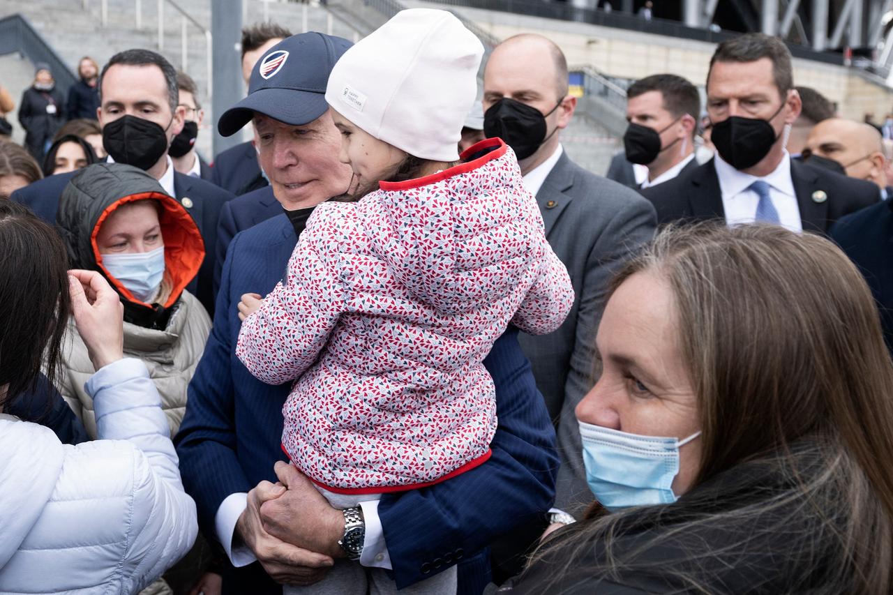 US-Präsident Biden mit einem Mädchen auf dem Arm, umringt von Flüchtlingen und Bodyguards mit Mundschutz. US-Präsident Biden mit einem Mädchen auf dem Arm, umringt von Flüchtlingen und Bodyguards mit Mundschutz.