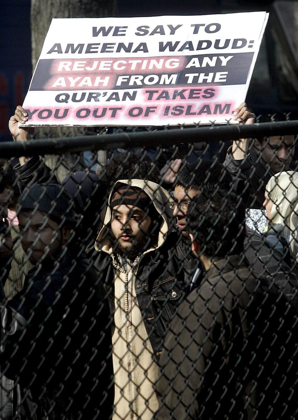 Hinter einem Zaun hält ein Mann mit beiden Armen ein Plakat in die Höhe, um gegen ein Freitagsgebet der Islamwissenschaftlerin Amina Wadud für Männer und Frauen zu protestieren. Hinter einem Zaun hält ein Mann mit beiden Armen ein Plakat in die Höhe, um gegen ein Freitagsgebet der Islamwissenschaftlerin Amina Wadud für Männer und Frauen zu protestieren.