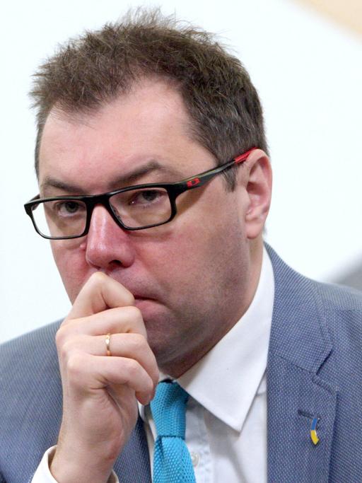 Das Bild zeigt eine Porträtaufnahme von Oleksii Makeiev, der seine Hand in einer nachdenklichen Geste vor Kinn und Mund hält.