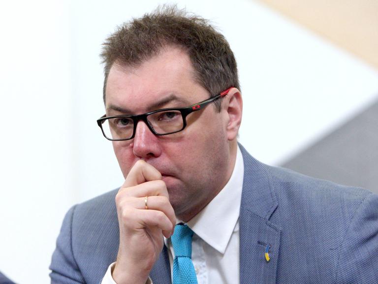 Das Bild zeigt eine Porträtaufnahme von Oleksii Makeiev, der seine Hand in einer nachdenklichen Geste vor Kinn und Mund hält.