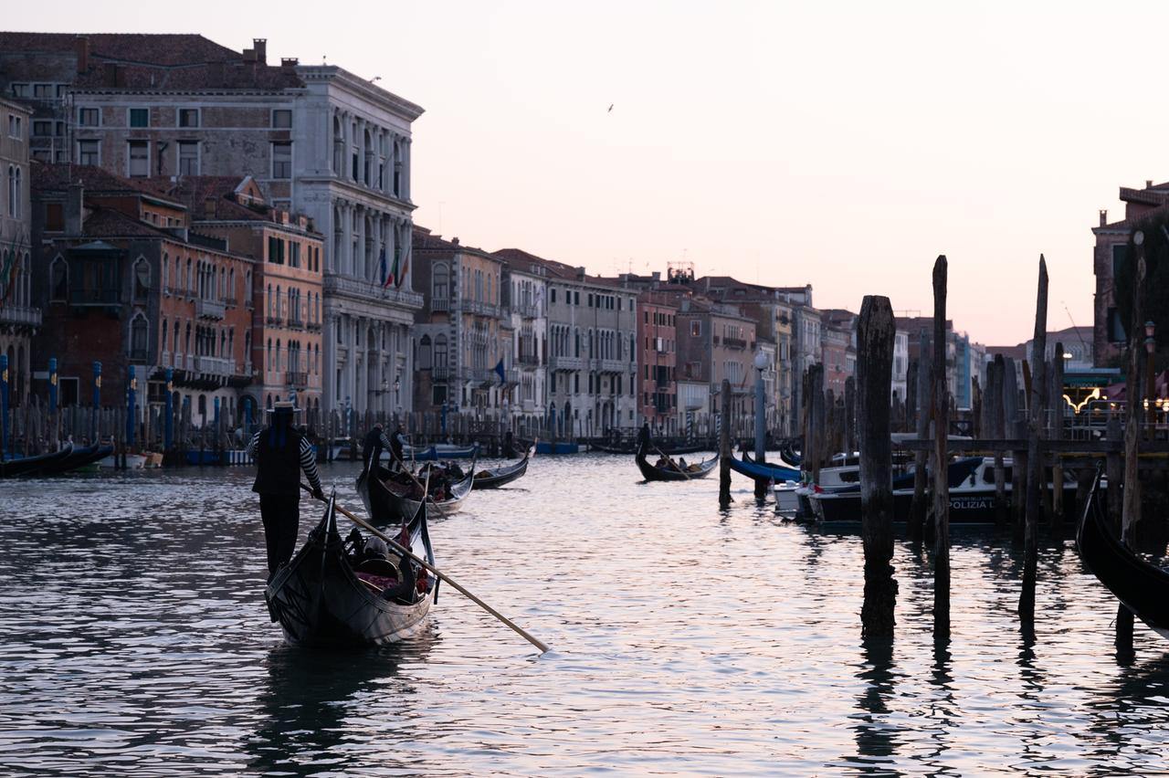 Ein Gondolieri steuert eine Gondel auf der Wasserstraße Canal Grande in Venedig bei Sonnenuntergang.