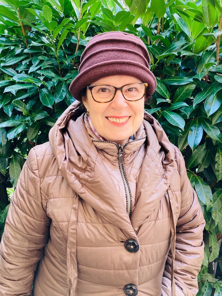 Porträt von Judith Landshut vor einem Busch mit grünen Blättern. Sie trägt eine Brille und einen Hut. Porträt von Judith Landshut vor einem Busch mit grünen Blättern. Sie trägt eine Brille und einen Hut.