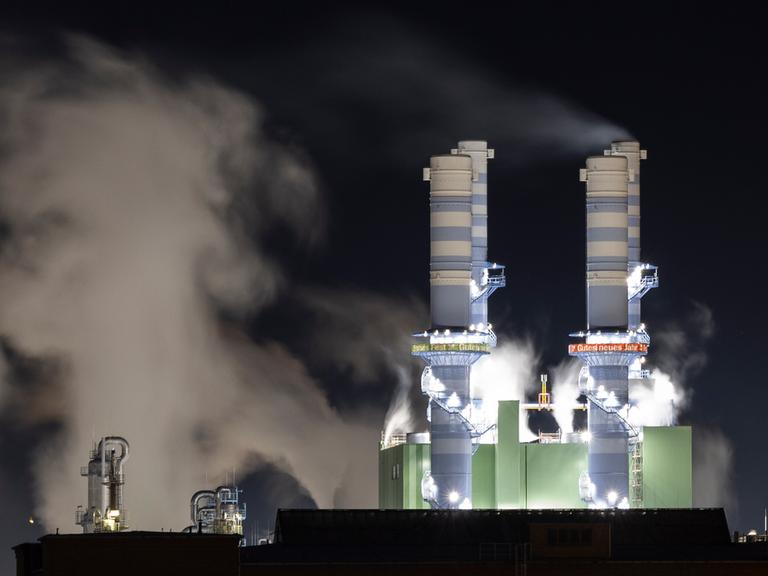 Dampf steigt bei Nacht aus beleuchteten Industrieschornsteinen des Industriepark Höchst auf. 