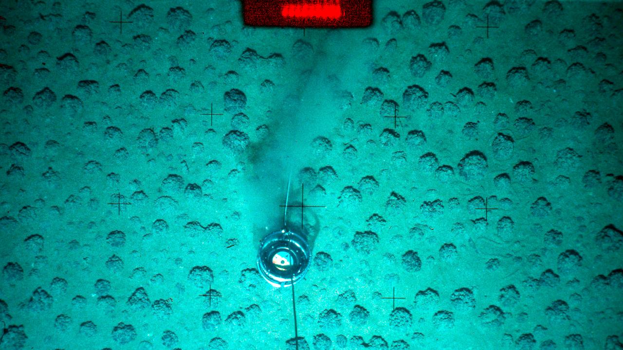 Manganknollen am Meeresboden in einer Tiefe von mehreren tausend Metern, die in ein türkises Licht getaucht sind. 