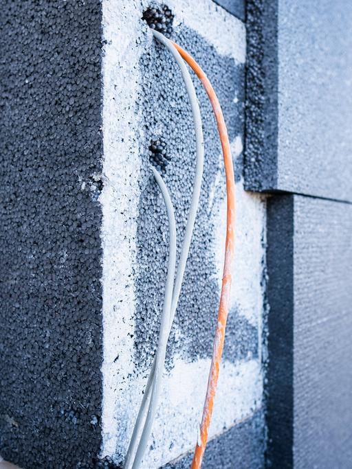 Dämmplatten an einer Hausfassade mit hervorschauenden blauen und gelben Kabeln.