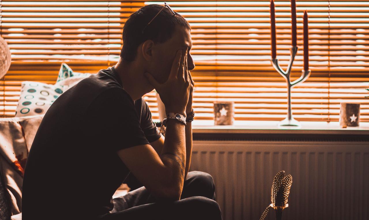 Ein Mann sitzt in einem verdunkelten Zimmer und hat seinen Kopf in den Händen aufgestützt. Ein Mann sitzt in einem verdunkelten Zimmer und hat seinen Kopf in den Händen aufgestützt.