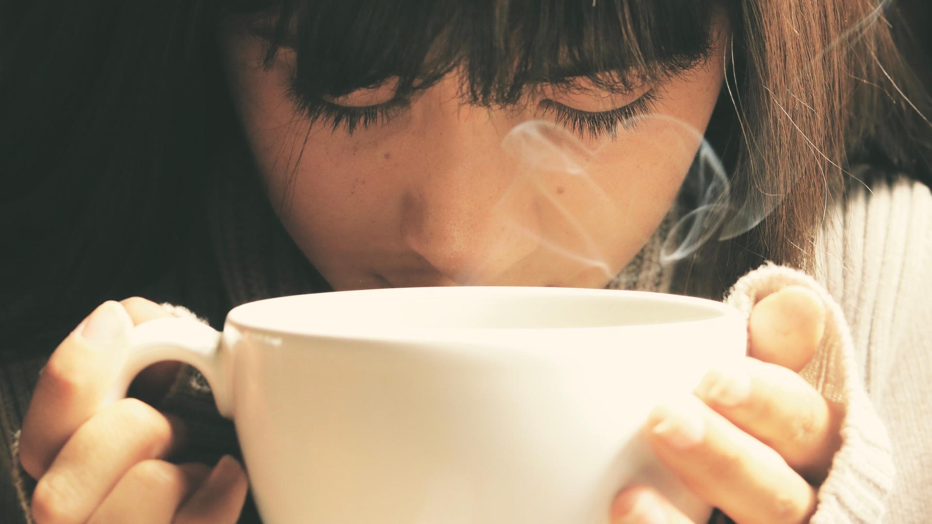 Eine junge Frau hält mit beiden Händen eine Tasse Tee in den Händen, aus der zufällig Dampf in Herzform aufsteigt. Eine junge Frau hält mit beiden Händen eine Tasse Tee in den Händen, aus der zufällig Dampf in Herzform aufsteigt.