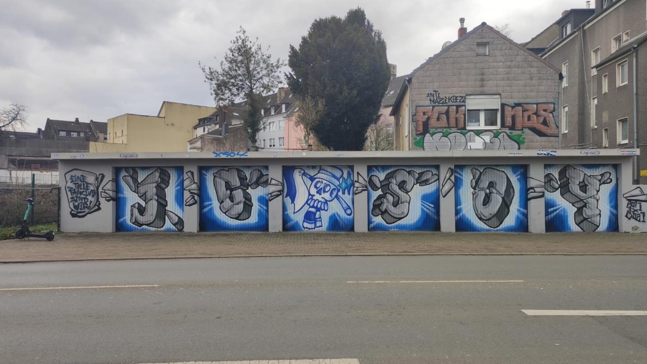 Stadtansicht von Gelenkirchen. Vor grauen Kleinstadt-Fassaden ist auf einer Garage ein Grafito eines Schalker Fanclubs zu sehen. Stadtansicht von Gelenkirchen. Vor grauen Kleinstadt-Fassaden ist auf einer Garage ein Grafito eines Schalker Fanclubs zu sehen.