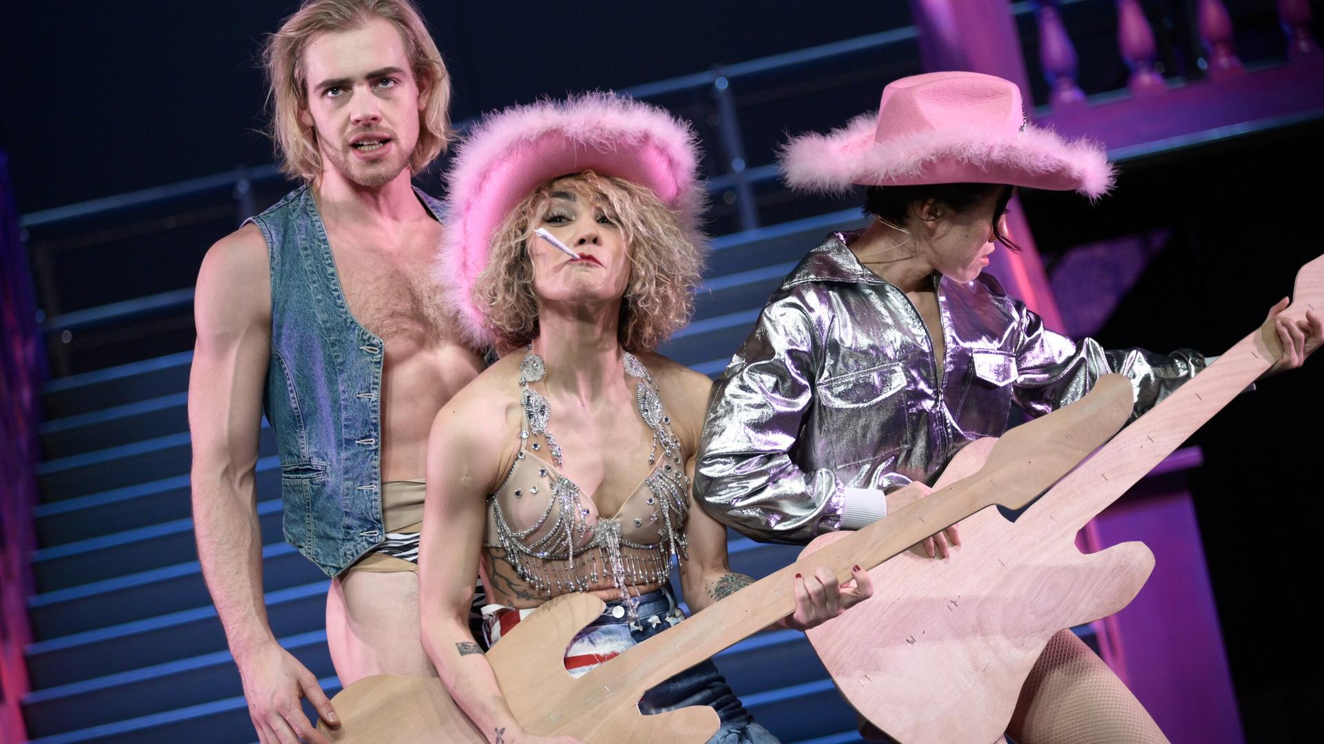 Die Tänzer tragen glitzernde Cowboystiefel und Cowboyhüte mit Federn und spielen Fake-Gitarren aus Holz. Die Tänzer tragen glitzernde Cowboystiefel und Cowboyhüte mit Federn und spielen Fake-Gitarren aus Holz.