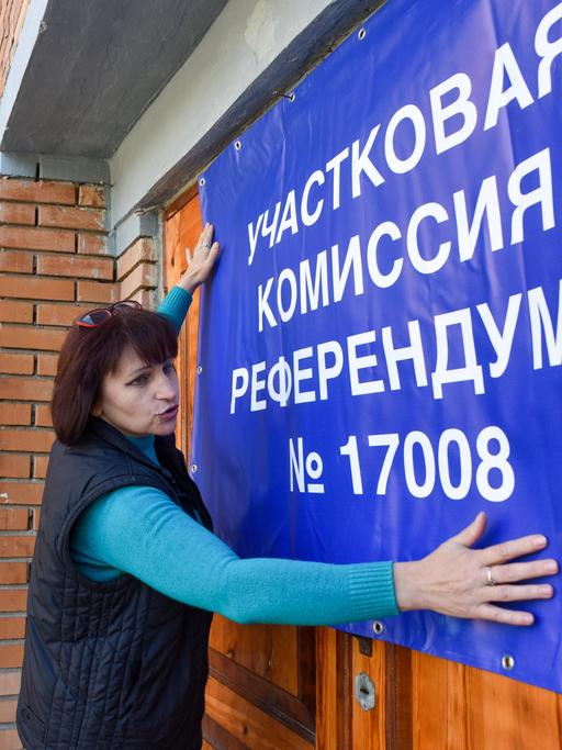 Eine Frau hängt ein Banner für das Scheinreferendum in Donezk auf. 