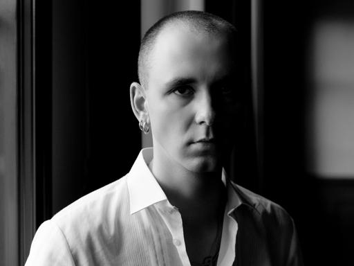 Drangsal, bürgerlicher Name Max Gruber, steht auf dem Schwarzweißbild in einem Innenraum und schaut in die Kamera. Er hat sehr kurze Haare, trägt ein weißes Hemd sehr weit aufgeknöpft. Sein Gesicht und Körper ist von links beleuchtet, die rechte Seite verschwimmt im Schatten.