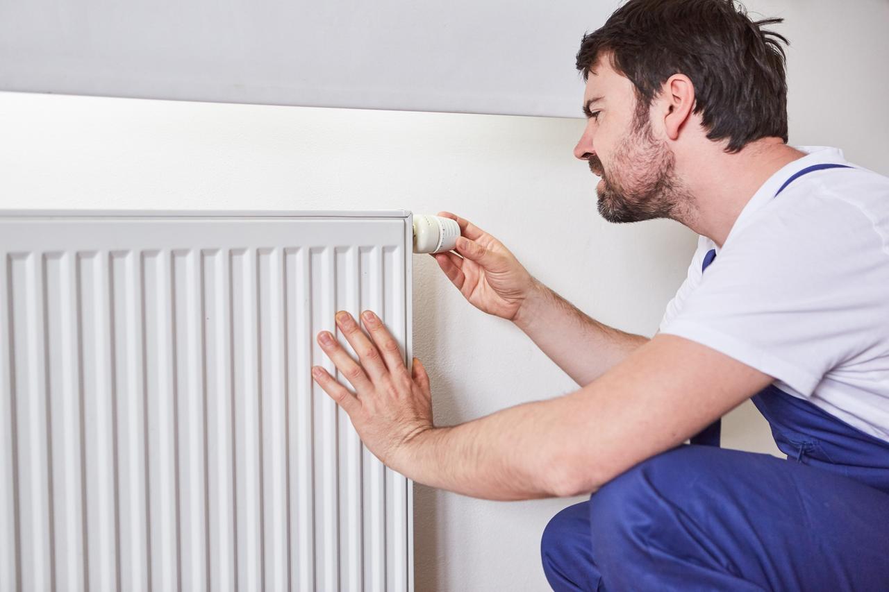 Ein Installateur justiert den Thermostat an einem Heizkörper. Ein Installateur justiert den Thermostat an einem Heizkörper.