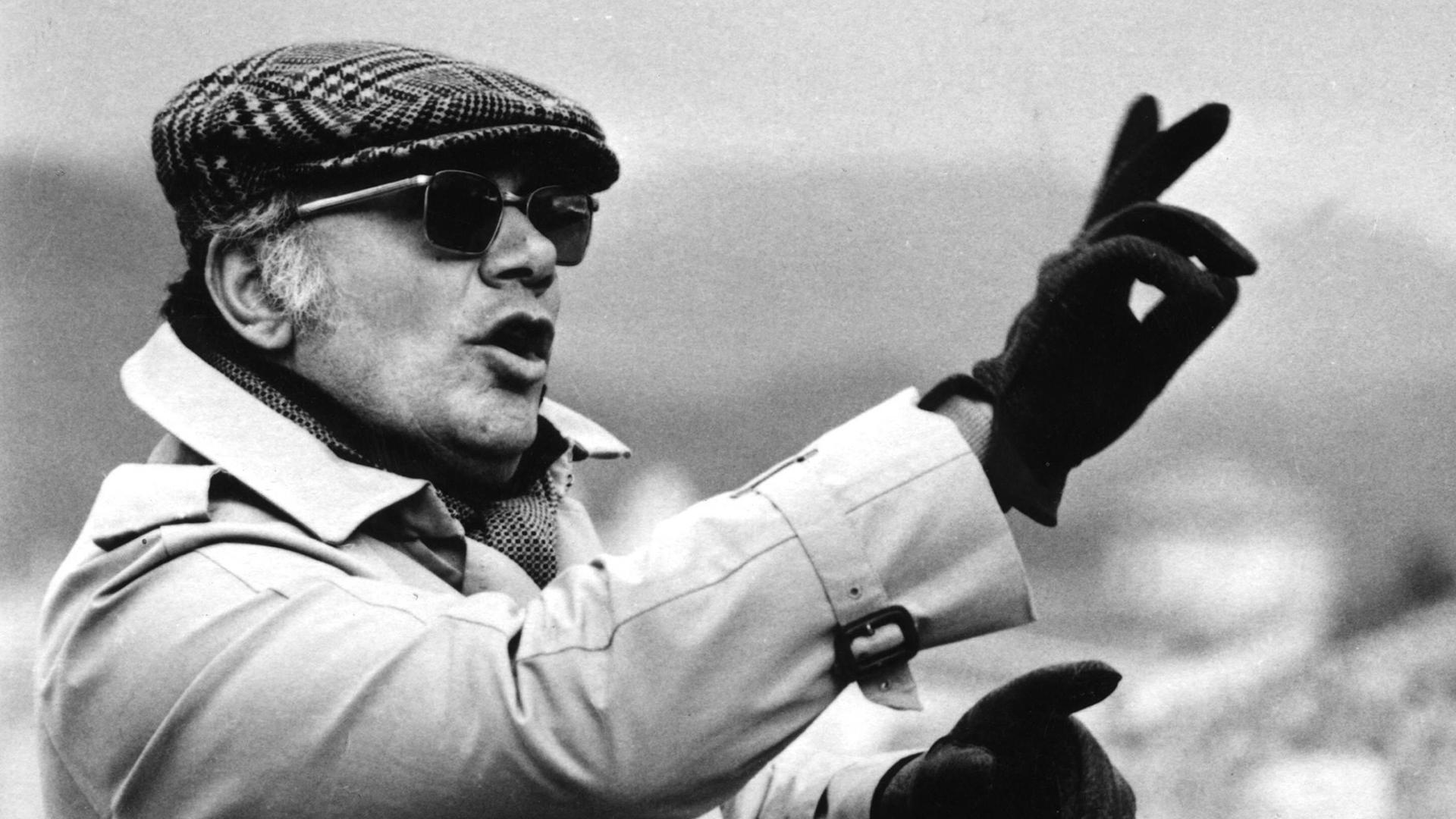 Der italienische Filmregisseur und Drehbuchautor Francesco Rosi gestikuliert und trägt eine Mütze, Sonnenbrille, Handschuhe und einen Regenmantel in den 1970er-Jahren Der italienische Filmregisseur und Drehbuchautor Francesco Rosi gestikuliert und trägt eine Mütze, Sonnenbrille, Handschuhe und einen Regenmantel in den 1970er-Jahren